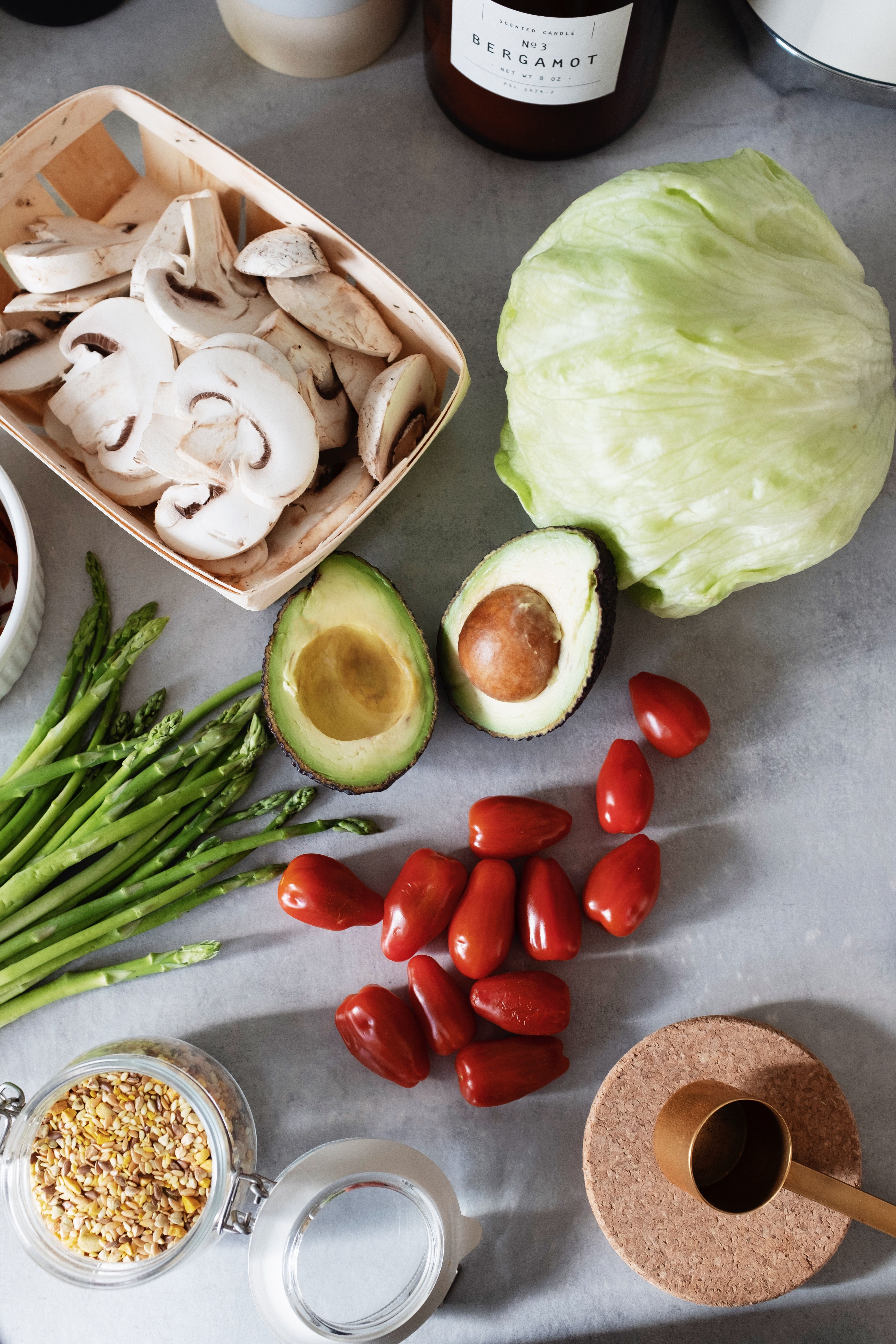 Fresh vegetables and healthy ingredients laid out on a table — mushrooms, avocado, asparagus, cherry tomatoes, cabbage, and grains